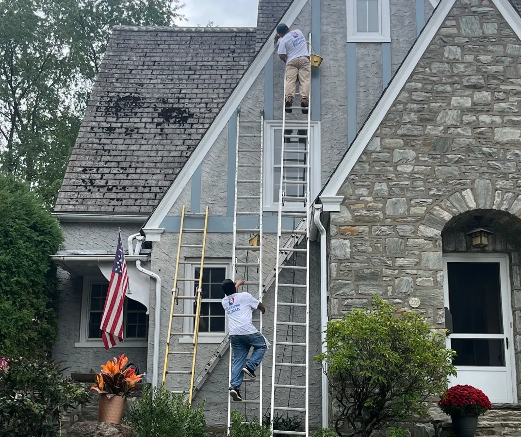 LX Pro Home painters on ladders working on the gables of a stone home exterior